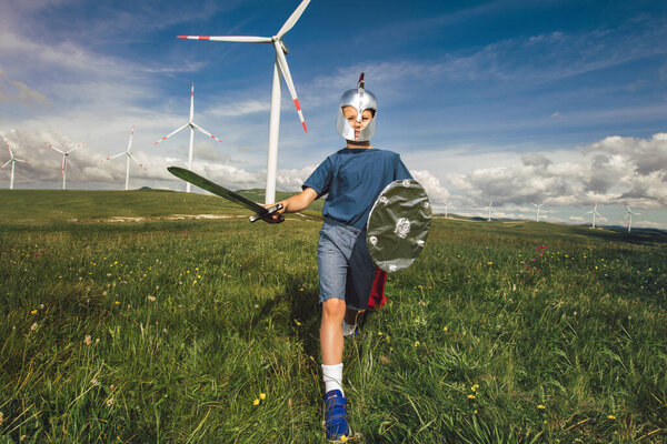 Little boy hold toy sword playing is in front of the wind farm