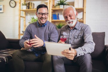 Portrait of senior man with adult son using digital tablet at home