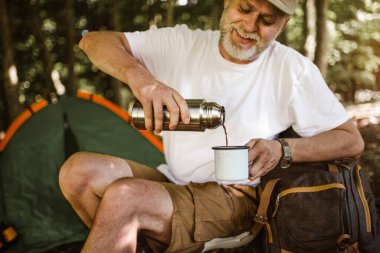 Doğada kamp yapan adam dinleniyor ve taze kahve içiyor.