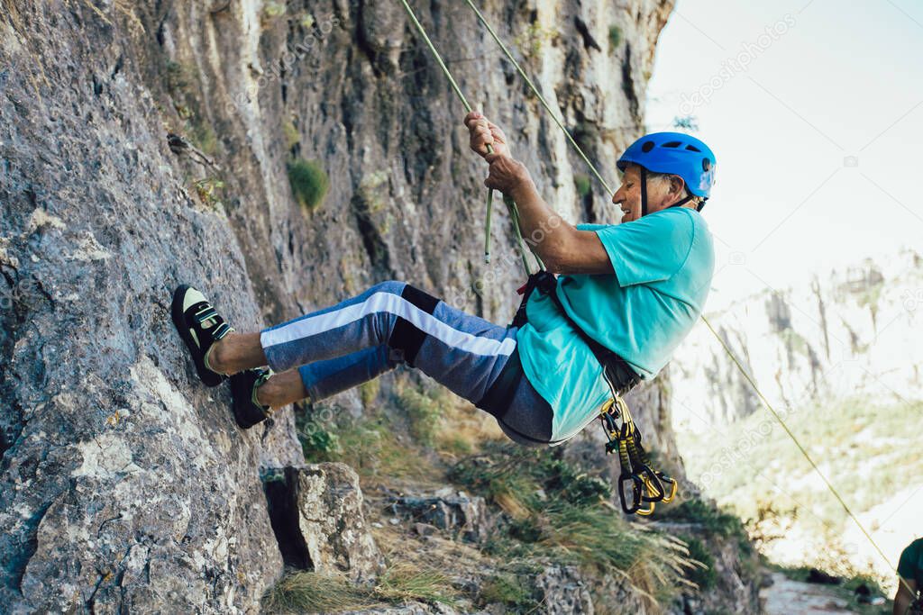 Senior man with a rope climbing on the rock.