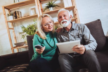 Üst düzey çift koltukta oturup televizyon seyrediyor, ellerinde dijital tablet var. Karantina altında.. 