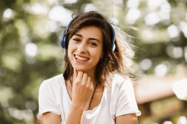 Heyecanlı kız müzik dinliyor. Kulaklıkları sokakta, saçları hareket ediyor.