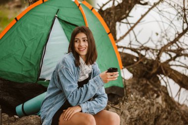 Genç bir kadın çadırın önünde oturmuş çay içiyor..