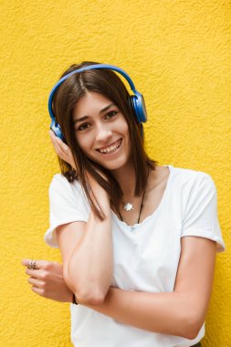 Kulaklıkla müzik dinleyen güzel bir kadının portresi. Sarı arkaplan.