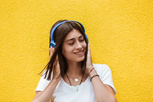 Portrait of beautiful woman joyful listening to music on headsets. Yellow background.