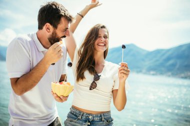 Genç mutlu çift sahilde meyvelerle eğleniyor.