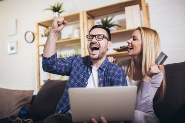 Mutlu çift evden alışveriş için kredi kartı ve laptop kullanırken iletişim kuruyor..