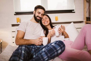Genç mutlu çift sabahları yatakta kahve içiyor.