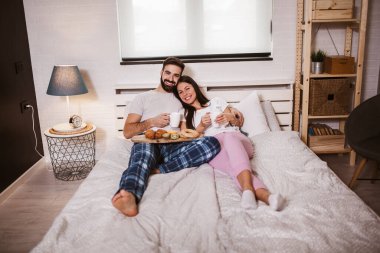 Genç mutlu çift sabahları yatakta kahve içiyor.