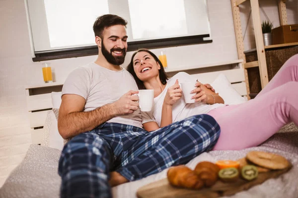 在床上微笑的年轻夫妇喝咖啡 互相望着对方 — 图库照片