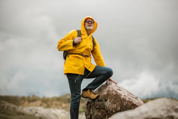 レインコートとバックパックで山の景色を楽しむ中世の男性旅行者 — ストック写真