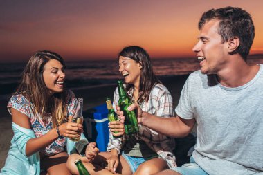 Mutlu arkadaşlar sahilde içkilerle parti yapıyorlar. Mutlu gençler plaj partisinde eğleniyor, birlikte kutluyorlar..