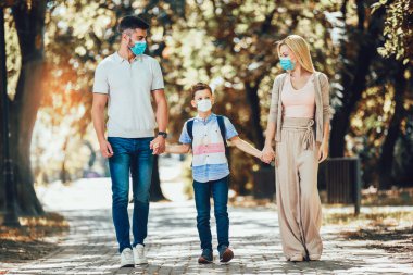 Anne, baba ve küçük oğlu parkta virüs hastalığından korunmak için yüz koruyucu maske takıyor..