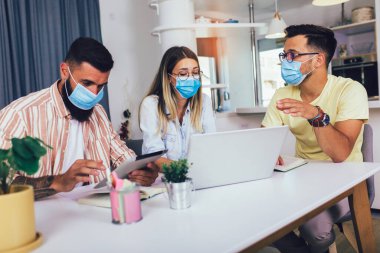 Öğrenciler evde çalışır, koruyucu maskeler takar ve dizüstü bilgisayar kullanır.