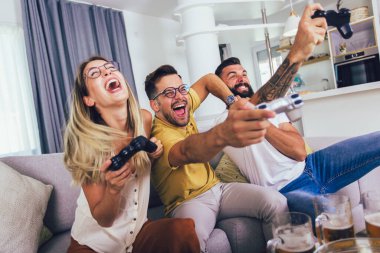 Bir grup arkadaş oturma odasında kanepede oturup video oyunu oynayarak eğleniyorlar..