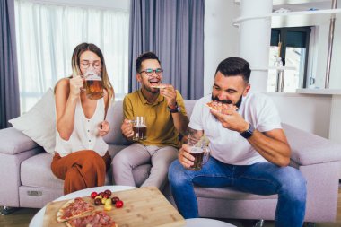 Bir grup genç birlikte eğleniyor. Bira ve pizzayla aydınlık bir odada oturmak..
