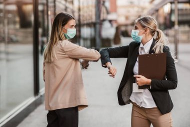 Güvenlik maskeli iş kadınları ofis binasının önünde dirsekleriyle selam veriyorlar.. 