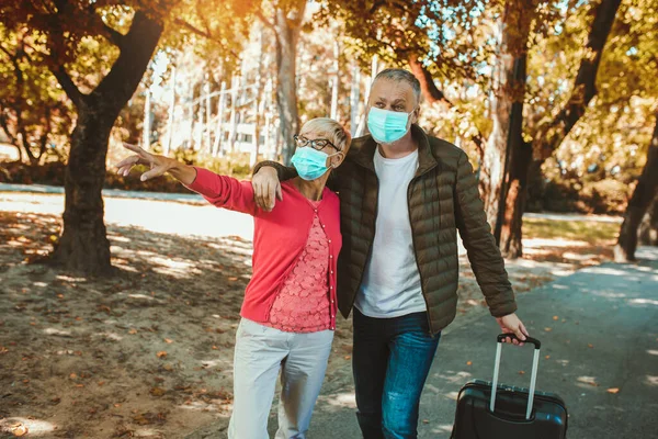 Seniorenpaar Mit Schutzmaske Zieht Koffer Auf Reise — Stockfoto