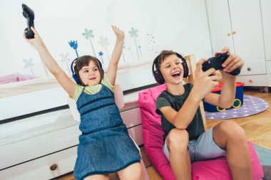 Güzel küçük kız ve oğlan oyun konsolu oynuyor ve evde gülüyorlar.