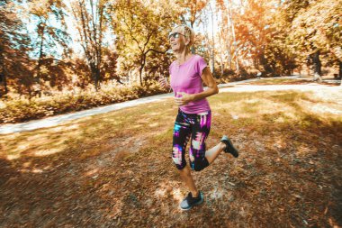 Yaşlı bir kadın parkta kulaklıkla koşuyor.