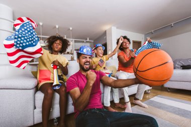 Üç kişilik mutlu Afro-Amerikan ailesi televizyon izliyor ve evdeki kanepede basketbol maçlarına tezahürat yapıyor..