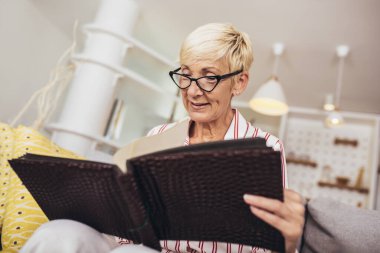 Neşeli, son sınıf öğrencisi, elinde aile fotoğrafı albümüyle evdeki kanepede oturuyor.