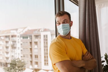 Coronavirus salgını covid-19 ve karantina konsepti. Pencerenin yanındaki tıbbi maskeli adam.
