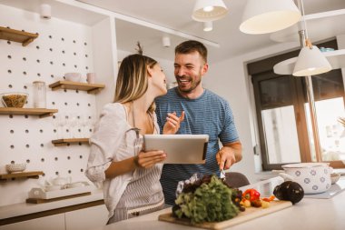Genç çift mutfakta birlikte yemek pişiriyor. Dijital tablette yemek tarifleri okuyorlar..