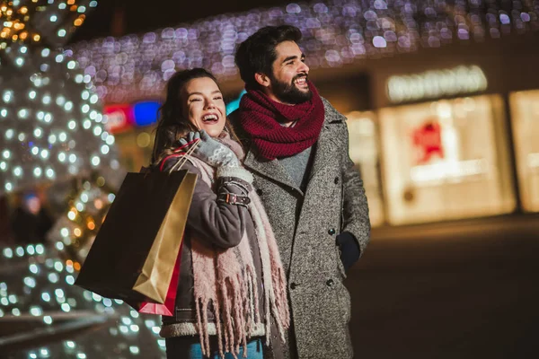市内中心部の若いカップルが休日の明るさを背景にしています クリスマスの夜に贈り物を持っているカップル — ストック写真