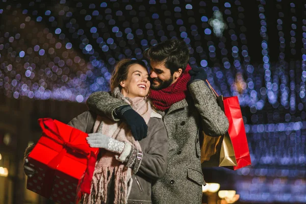 Young couple in the city centre with holiday\'s brights in background. Couple holding gift in a Christmas night.