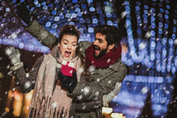 Young couple outdoor with holiday\'s brights in background. Man presenting gift to woman.