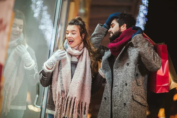 夕方に街を歩く中でクリスマスライトの背景にギフトバッグを持つカップル ウィンドウショッピング — ストック写真