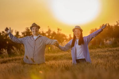 Taylandlı bir kadın ve yaşlı bir çiftçi gün batımında altın buğday tarlasında el ele tutuşuyorlar, ekinlerinin gelişmesinden, tarımın ve kırsal yaşamın sergilenmesinden memnunlar..