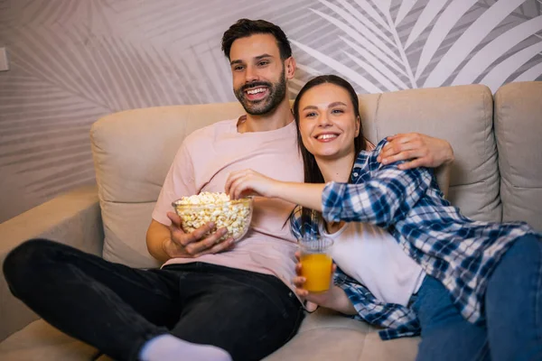 Genç çift oturma odasında uzanıp sarılıyor, televizyon izliyor, patlamış mısır yiyor, meyve suyu içiyor, gülümsüyor ve en sevdikleri dizinin tadını çıkarıyor..