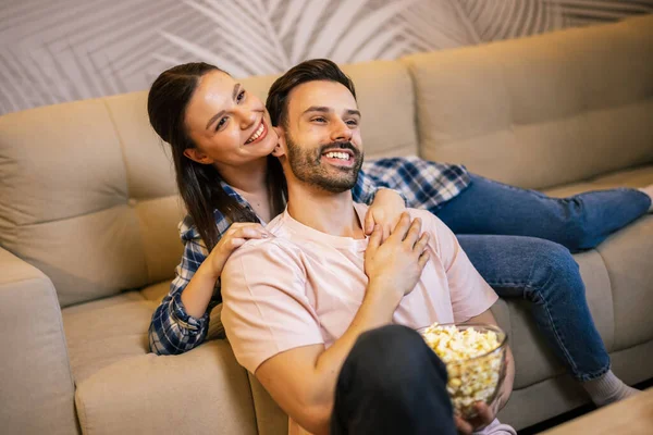 Genç çift oturma odasında uzanıp sarılıyor, televizyon izliyor, patlamış mısır yiyor, meyve suyu içiyor, gülümsüyor ve en sevdikleri dizinin tadını çıkarıyor..