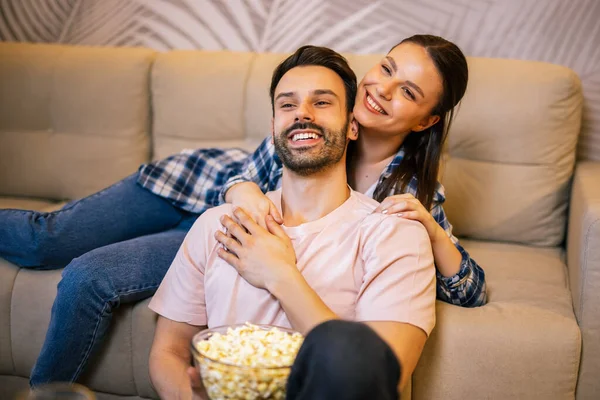 Genç çift oturma odasında uzanıp sarılıyor, televizyon izliyor, patlamış mısır yiyor, meyve suyu içiyor, gülümsüyor ve en sevdikleri dizinin tadını çıkarıyor..