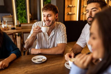 Bir grup genç arkadaş modern kafede eğleniyor, sohbet ediyor ve sosyal ortamlarda rahatlıyorlar..