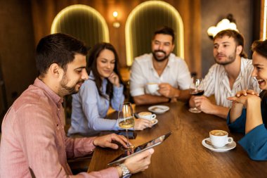 Bir grup genç arkadaş modern kafede eğleniyor, sohbet ediyor ve sosyal ortamlarda rahatlıyorlar..