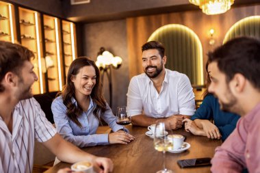 Bir grup genç arkadaş modern kafede eğleniyor, sohbet ediyor ve sosyal ortamlarda rahatlıyorlar..