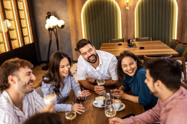 Modern restoranda gülümseyen ve şarap içen bir grup genç arkadaş, neşeli bir sosyal an..