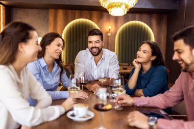 Modern restoranda gülümseyen ve şarap içen bir grup genç arkadaş, neşeli bir sosyal an..