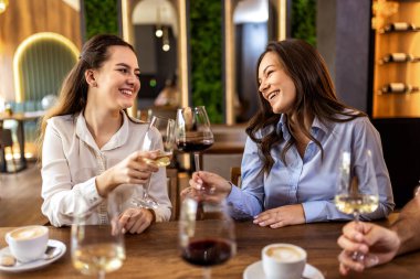 Modern kafede gülümseyen ve kadeh tokuşturan iki genç kadın, neşeli ve kutlama anı.