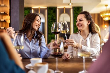 Modern kafede gülümseyen ve kadeh tokuşturan iki genç kadın, neşeli ve kutlama anı.