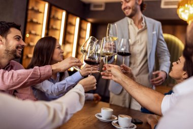 Bir grup genç arkadaş modern kafede kadeh kaldırırken bir adam ayakta duruyor, neşeli sosyal an..