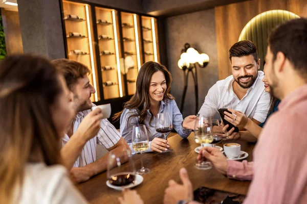 Modern restoranda gülümseyen ve şarap içen bir grup genç arkadaş, neşeli bir sosyal an..