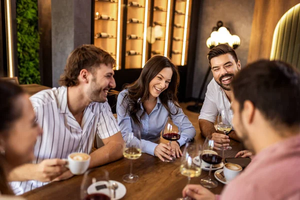 Modern restoranda gülümseyen ve şarap içen bir grup genç arkadaş, neşeli bir sosyal an..