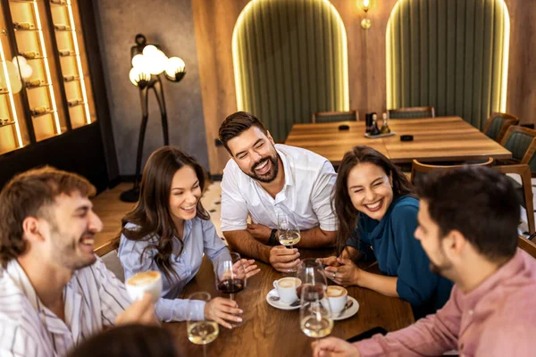 Modern restoranda gülümseyen ve şarap içen bir grup genç arkadaş, neşeli bir sosyal an..