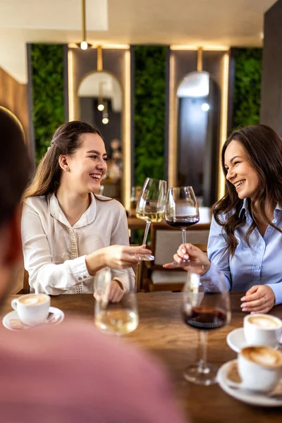 Modern kafede gülümseyen ve kadeh tokuşturan iki genç kadın, neşeli ve kutlama anı.