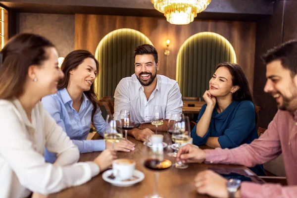 Modern restoranda gülümseyen ve şarap içen bir grup genç arkadaş, neşeli bir sosyal an..