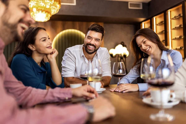 Modern restoranda gülümseyen ve şarap içen bir grup genç arkadaş, neşeli bir sosyal an..